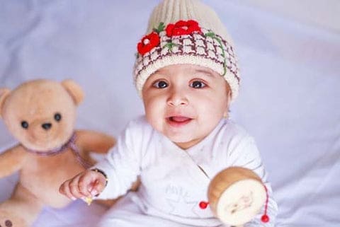 Un bébé dans son lit avec un petit bonnet trop chou et son doudou